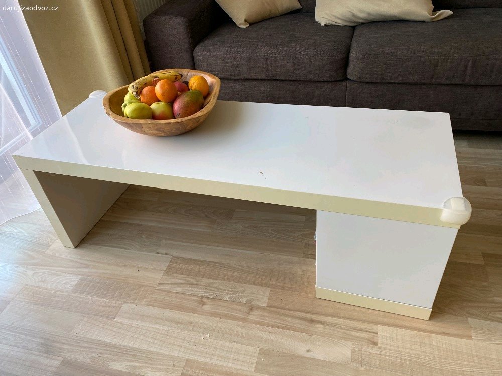 Konferenční stolek. Chtel bych darovat  konferencni stolek (120x42x40 cm)-ma drobne vady (viz foto). Material je laminovana deska -drevotriska v bile leskle barve.
Vzhledem ke sve vysce ho lze vyuzit i jako detsky stolek. Ma prihradku na casopisy/knihy.
Pouze osobni predani v Hostivici nebo Praha 13.