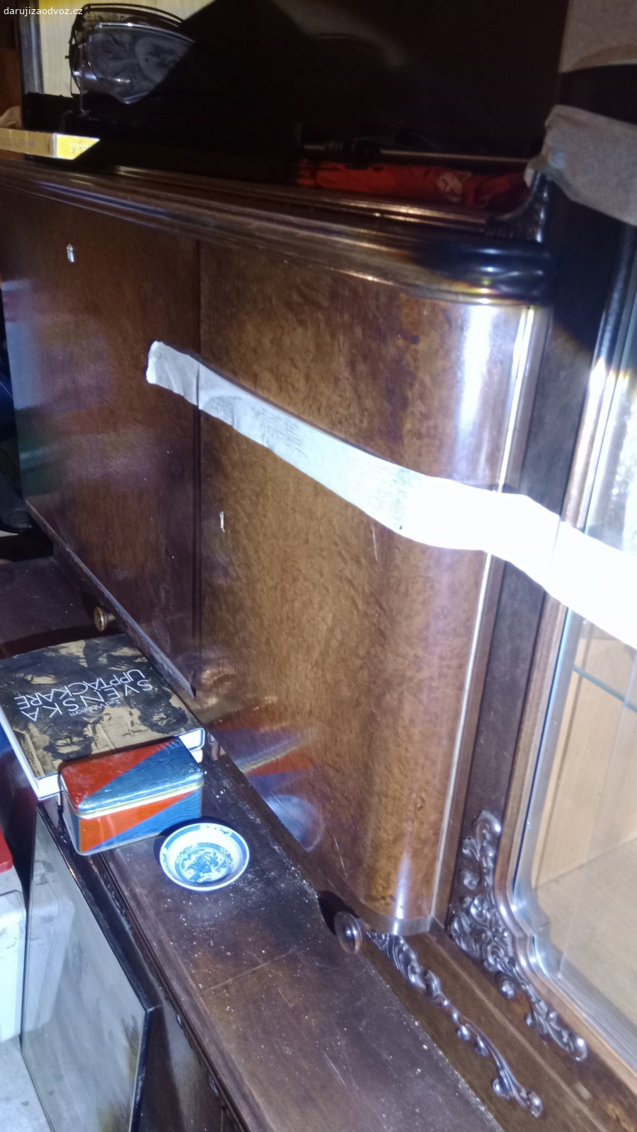 Krásná vitrína prvorepubliková. Má (nejspíš) řezbované detaily.
roh vitríny je z oblého skla.
Pěkná práce. 
To není IKEA, to Vás přežije ??
Za odvoz ?