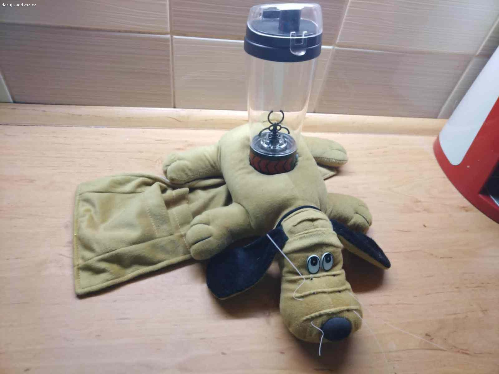 Retro pejsek na pohovku – držák na ovladače a pití. Daruji (třeba ovoce pro děti potěší - není podmínkou) textilní držák / organizér na pohovku nebo křeslo na opěradlo, ve tvaru pejska. 
Praktický i dekorativní doplněk k televizi, třeba na ovladače.
Pejsek je uvnitř vyplněn zátěží, díky které stabilně drží na okraji pohovky nebo křesla bez nutnosti uchycení.
Uprostřed má kruhový otvor na láhev nebo sklenici a po stranách kapsy na uložení až dvou dálkových ovladačů nebo drobností - viz  foto.
Předám bez obsahu ( lahev - šejkr už není) v Praze 10-Strašnice.