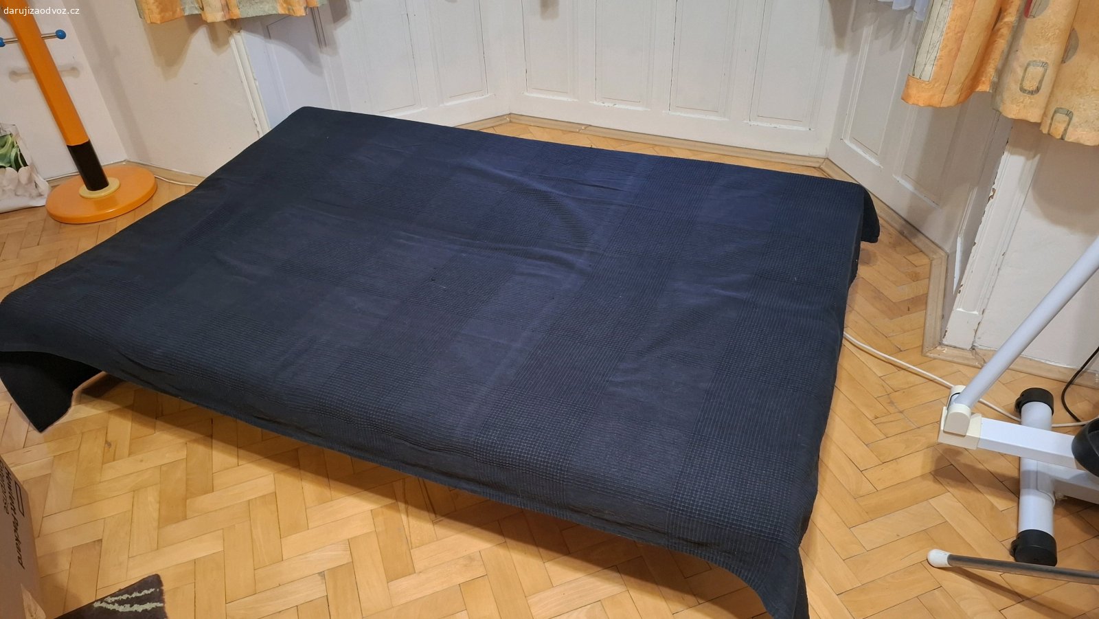 Rozkládací gauč. Na železné konstrukci je lamelový rošt a na něm dvoudílná molitanová matrace a černý přehoz. Rozměry 180x60cm, rozložený 180x120cm