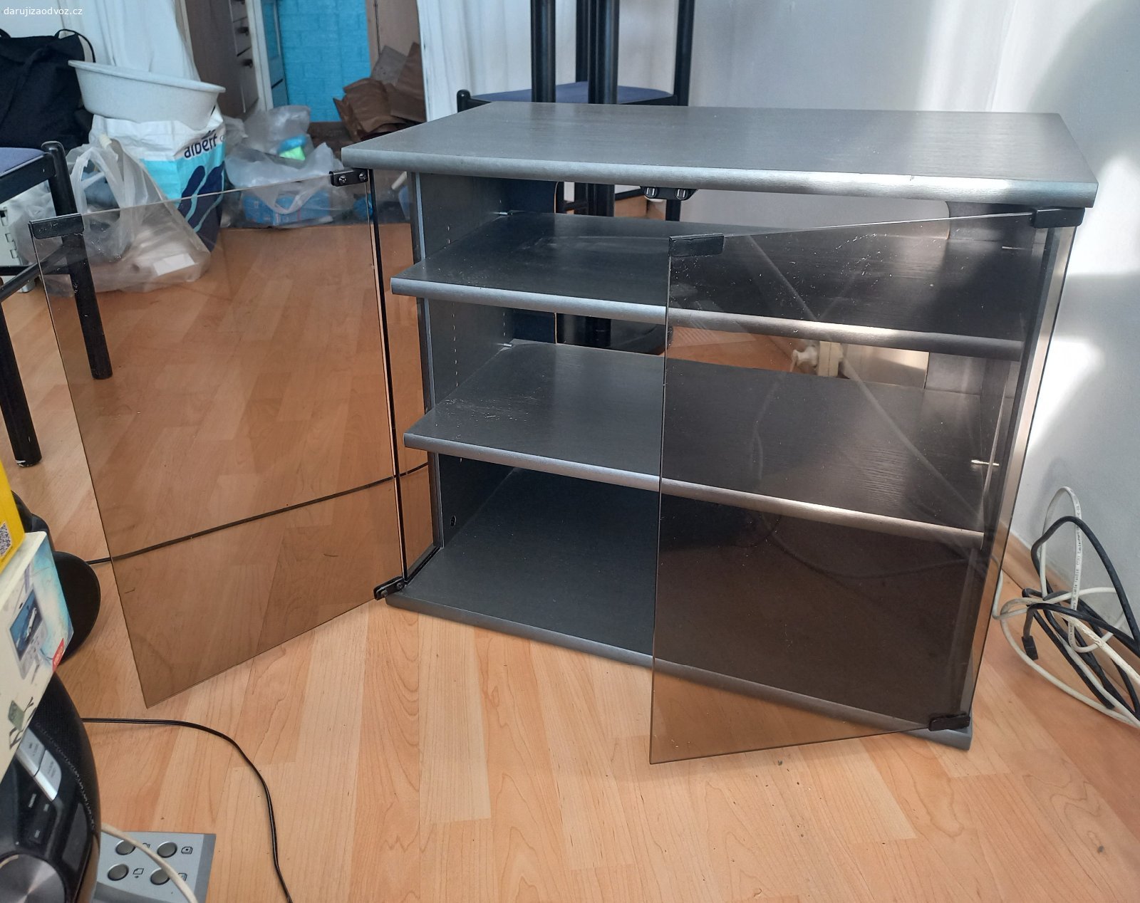 Skříňka pod TV s poličkami pro audio - video. Skříňka s tmavým sklem, černostříbrným povrchem, elegantní.
Vhodná pod televizi, uvnitř poličky  pro audio - video přehrávače.
Bez zadní stěny, dobré pro vývod kabelů. 
Prosklená dvířka s magnetovým přiklepnutím. 
Spěchá, volejte na telefon.
